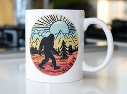 retro bigfoot colorful coffee mug stating  believe  with mountain and sunset background