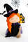 Felt Halloween toy - witch in the pointed hat with a broomstick standing in the background of painted Halloween decorations, left side view