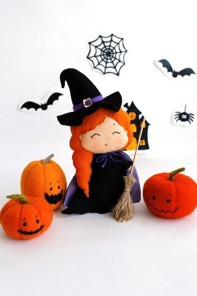 Felt Halloween toy - witch in the pointed hat with a broomstick with orange Halloween pumpkins standing in the background of painted Halloween decorations